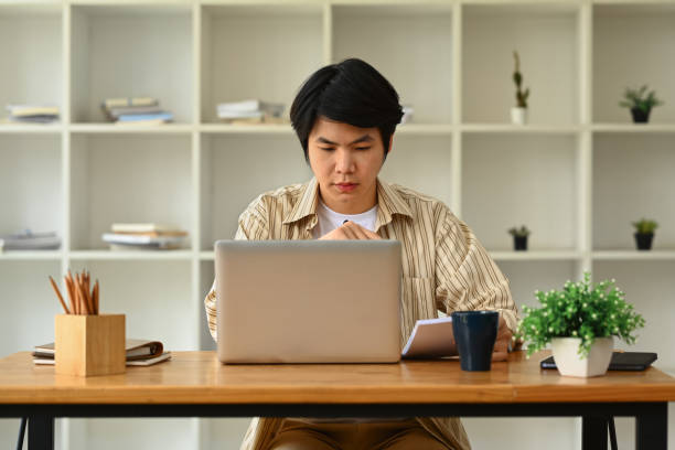 istock Focused asian male entrepreneur looking at computer screen and writing important notes. 1499139897