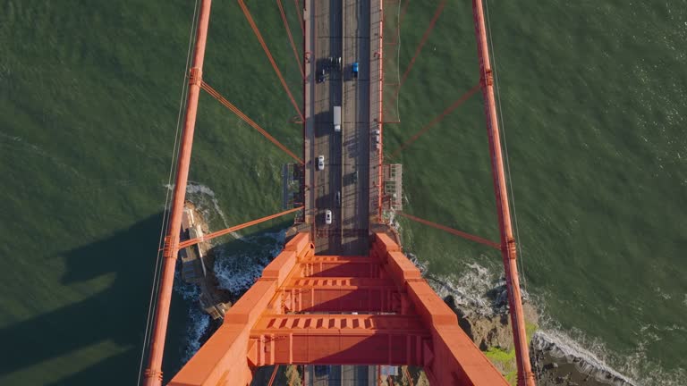 Top down view of traffic on Golden Gate Bridge in late afternoon sunshine. Fly over tower of large suspension bridge. San Francisco, California, USA