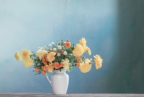 yellow and white chrysanthemum in white jug on wooden table