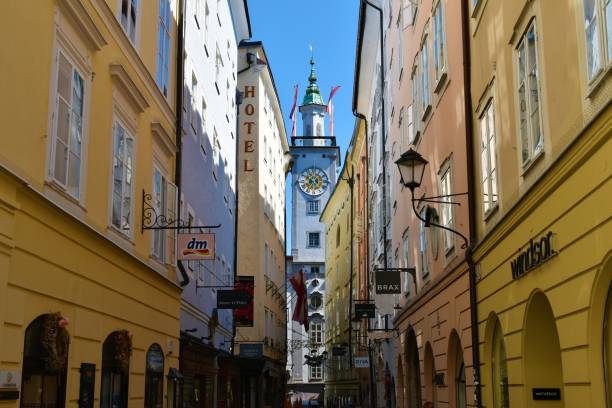 enge straße in salzburg, österreich und ein turm mit einer uhr der katholischen kirche der kollegienkirche - kollegienkirche stock-fotos und bilder