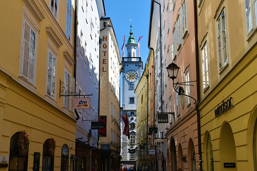 Salzburg, Austria - June 14 2023: Narrow street in Salzburg, Austria and a tower with a clock of the Kollegienkirche catholic church