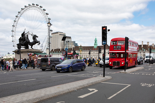 London, England; 06/06/2023: English double-decker bus crossing Westminster bridge with the ferris wheel \