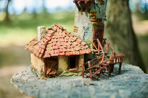 Little dollhouse in woods, cute small decorative house outdoor art exhibition in public park. Forest small doll house on forest background, charming garden decoration for home lawn,