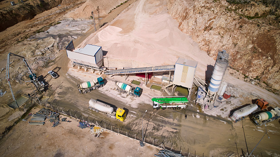 Aerial view of concrete mixing trucks and siloses of plant producing cement. Industrial concrete batching plant aerial view.