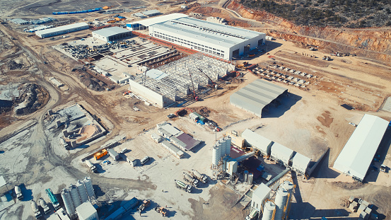 Prefabricated industrial buildings at construction site. Concrete foundations and metal frameworks of warehouses under construction