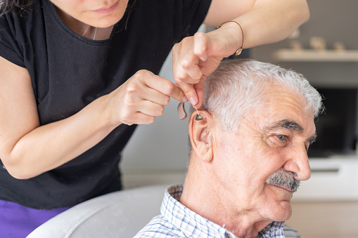 Caregiver İnserting Hearing Aid In Senior’s Ear