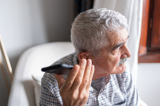 Senior Man With Hearing Aid Using Smartphone