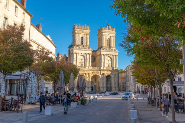 The Auch Cathedral steeples in France facing the sunset Auch, France - November 5, 2022: The Auch Cathedral steeples facing the sunset with some people sitting and walking on a busy commercial street sainte marie stock pictures, royalty-free photos & images