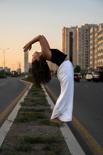 Young Asian woman practicing yoga outdoor during daytime with the view of the city. The girl performs a handstand at the column. Urban yoga, sunrise workout.