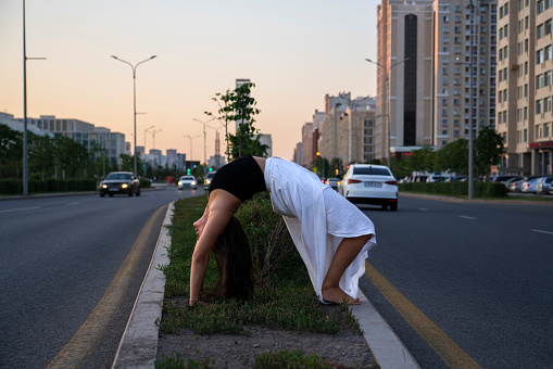 Young Asian woman practicing yoga outdoor during daytime with the view of the city. The girl performs a handstand at the column. Urban yoga, sunrise workout.