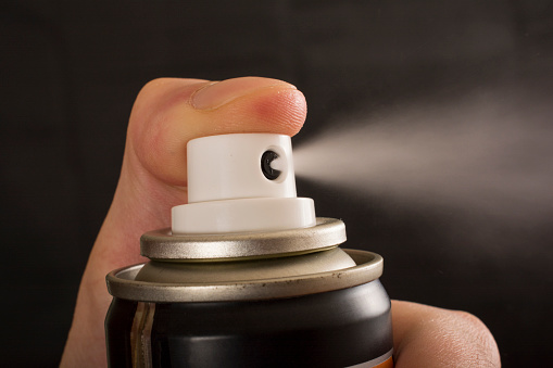 Close-up view of a human hand and pressed bottle of spray isolated on a black background