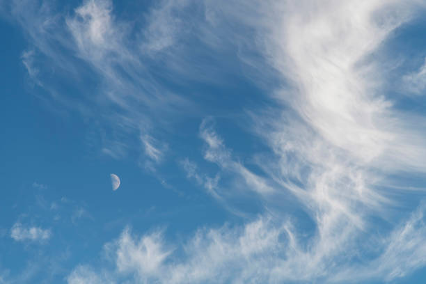 Image filling view of cirrus or feather clouds against a blue sky with a half moon between the clouds