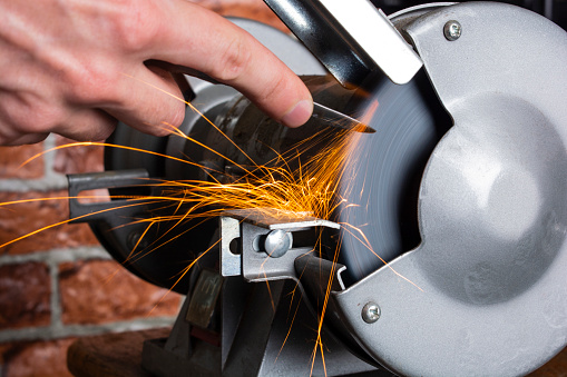 A knife sharpener and hand with a blade on a wooden table, close-up against a brick wall background