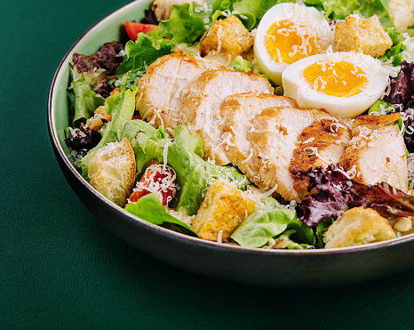 Caesar salad with chicken breast on green background