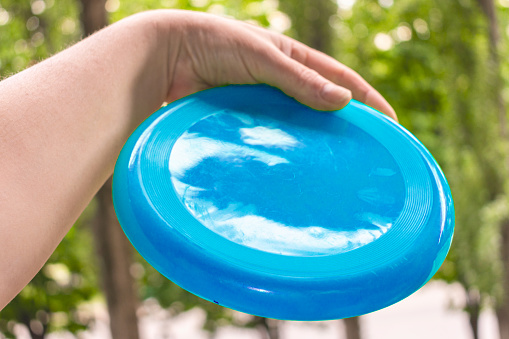 Happy man throws a flying disc in the park with his left hand away from himself on a sunny day