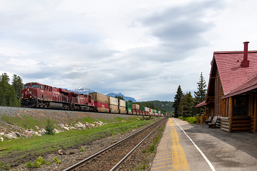 Lake Louise, AB, Canada-August 2022; View along the railway embankment along the former Lake Louise Railway Station with Canadian Pacific locomotives pulling cars with containers