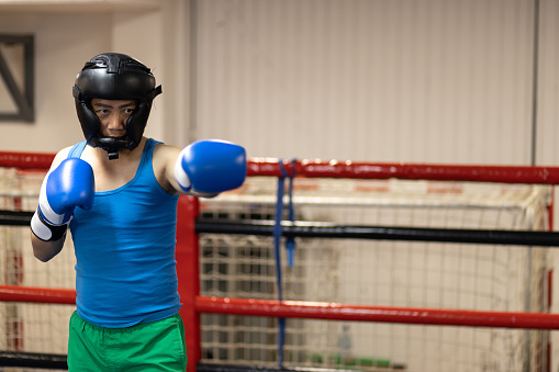 Young Chinese man going for boxing training. In this photo he is practicing punches in the boxing ring.