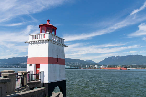 Vancouver, BC, Canada-July 2022; View of the 1914 built red and white striped square tower of Brockton Point Lighthouse in Stanley Park with North Vancouver and mountains in background