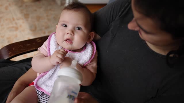 B-roll of baby girl drinking milk from the baby cup, while mother holding her