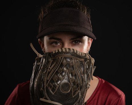 Athletic fast pitch softball player in red and black uniform shows only her eyes above her glove.