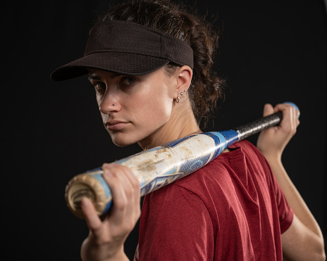 Athletic fast pitch softball player in red and black uniform has her composite bat resting across her shoulders.