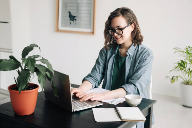 Young woman working on laptop in professional office setting. Student girl multitasking at home office. Work-from-home, freelance, business lifestyle concept. Technology, productivity and remote work. Young woman working on laptop in professional office setting. Student girl multitasking at home office. Work-from-home, freelance, business lifestyle concept. Technology, productivity, and remote work smart office stock pictures, royalty-free photos & images