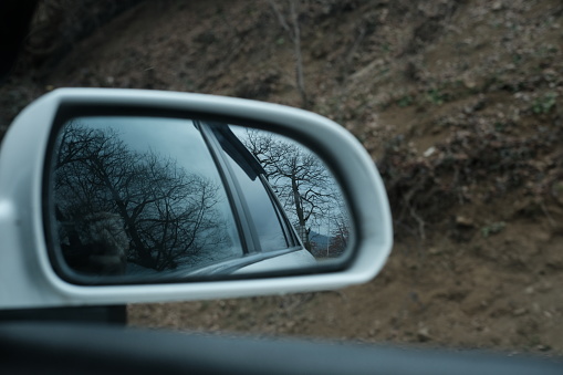 The view from the saloon of a vehicle moving in the winter season. Forest and mountain view reflected from car mirror