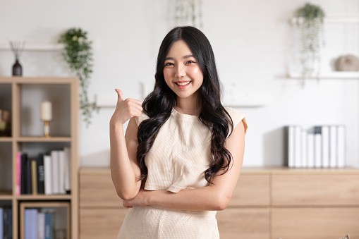 Beautiful young Asian woman showing thumbs up good gesture smile with positive emotional at home. Attractive female making finger thumbs up happiness and cheerful. Women lifestyle concept