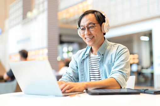 Smart confidence asian startup entrepreneur business owner businessman smile using laptop working online while listening music wireless headphone working relax leisure in cafe