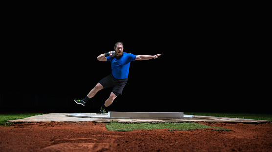 Athlete man throwing shot put ball on track during practice at night in athlete arena. Sport and healthy lifestyle concept.