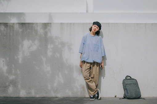 portrait Asian Chinese young woman looking at camera leaning on street wall waiting