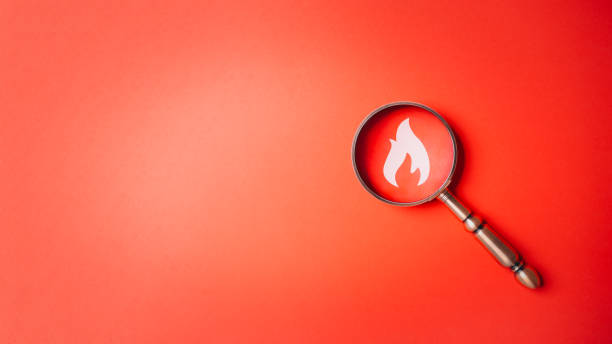 Fire surveillance inspection indicator and fire fighting with magnifying glass on red orange background. Fireman and conflagration concept. Wildfire and forest fire theme. stock photo