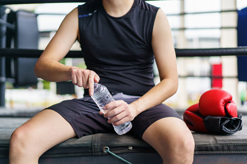 Active Asian sportsman relaxing and drinking water after have an indoor boxing at the boxing gym. Fitness portrait of good looking Asian sportsman doing a boxing workout - exercise in the indoor gym.