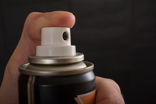 Close-up view of a human hand and pressed bottle of spray isolated on a black background