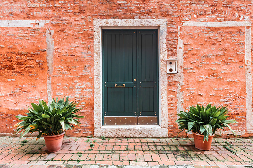 Red brick facade of the house with wooden door and flowers. Old medieval architecture in Venice, Italy.