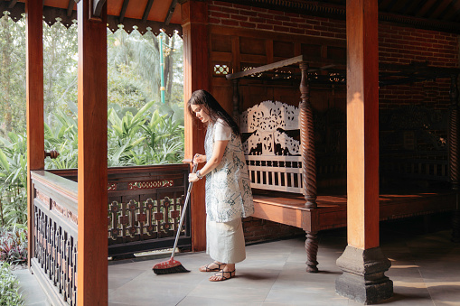 asian woman cleaning the floor of the  her  joglo house (a type of traditional vernacular house of the Javanese people) (Javanese omah)
