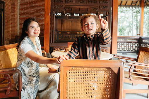 asian mother with her son (using surjan a Yogyakarta traditional clothes) sitting at their joglo house
