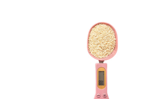 white sesame seeds in a pink electronic measuring spoon on a white background. - sesame seed spoon scoop imagens e fotografias de stock