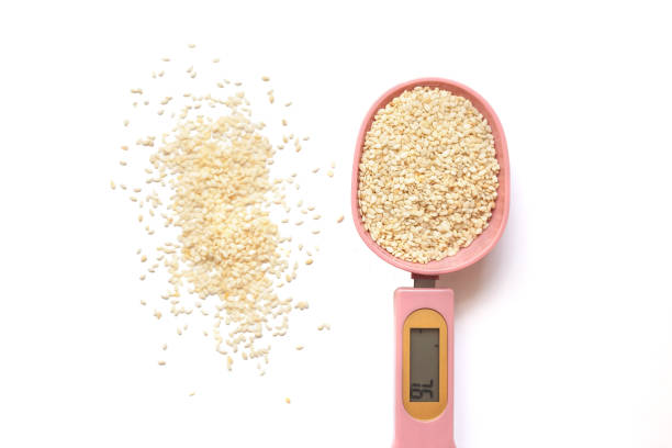 white sesame seeds in a pink electronic measuring spoon on a white background. - sesame seed spoon scoop imagens e fotografias de stock