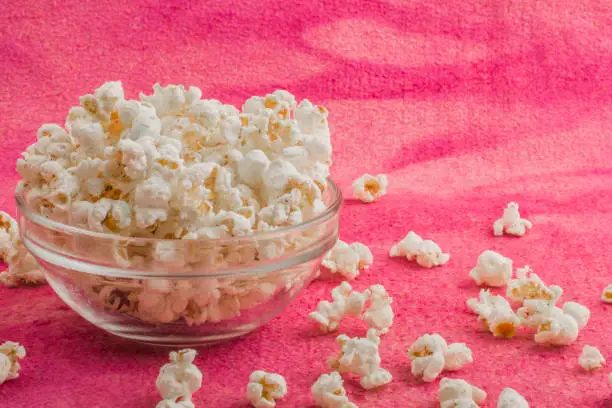 Photo of popcorn in a glass plate, on a pink background