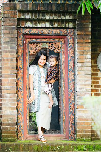asian mother with her son (using surjan a Yogyakarta traditional clothes) leaving  at their joglo house  (a type of traditional vernacular house of the Javanese people) (Javanese omah)