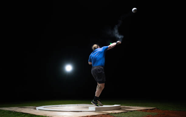 Athlete man throwing shot put ball on track during practice at night in athlete arena. Sport and healthy lifestyle concept.