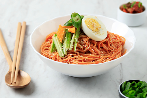 Bibim Guksu Naengmyeon, Korean Spicy Cold Noodle with Sliced Cucumber and Boiled Egg Topping. On White Marble Table