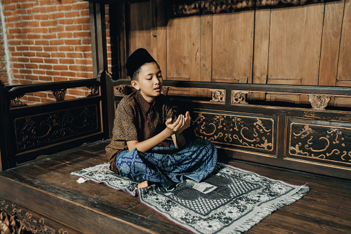 young muslim praying worship of the Allah's kindness  at  joglo house. Muslim children are doing prayers according to Islamic principles