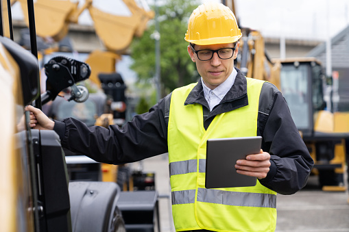 Worker in a helmet with a digital tablet on the background of construction machine.