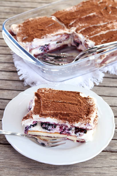 White ceramic cup holding a cocoa dusted dessert topped with raspberry and blueberries. Blurred background shows turquoise striped cups and napkins.