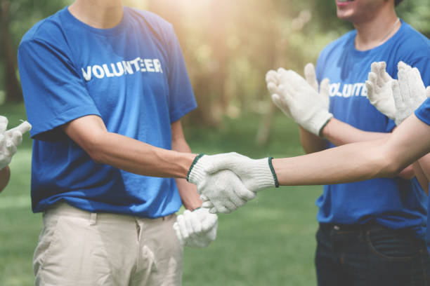 young asian volunteers handshake and working together at park area. ecology, charitable organization concept - wasting time imagens e fotografias de stock