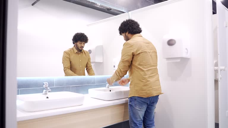 A young man washes his hands in a public toilet. Businessman in a shirt opened the tap with water in the wash basin,