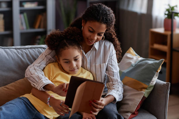 istock Loving mother and daughter using digital tablet together relaxing at home 1499252720