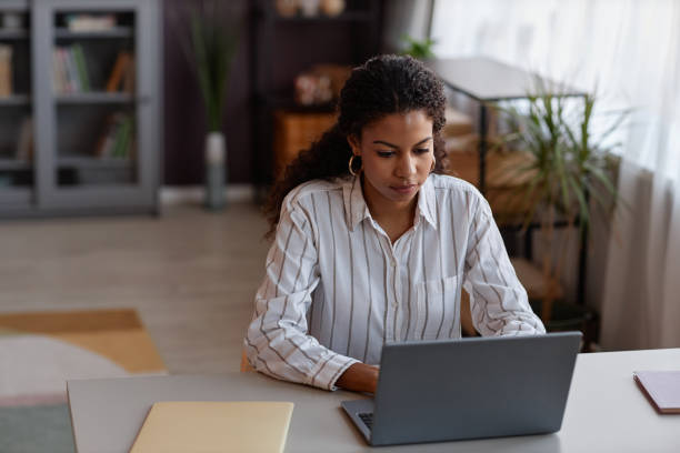 istock Black young woman using laptop working from home in cozy setting 1499252773